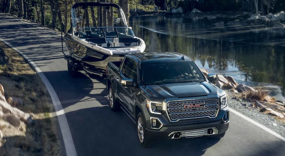 A black 2022 GMC Sierra 1500 towing a boat near a lake.