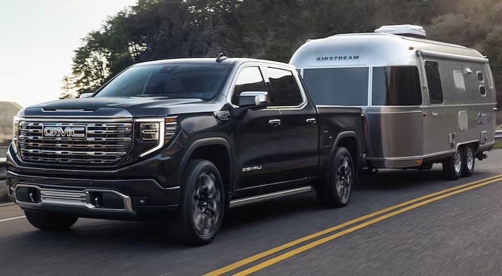 A black 2025 GMC Sierra 1500 Denali towing a trailer on a highway.