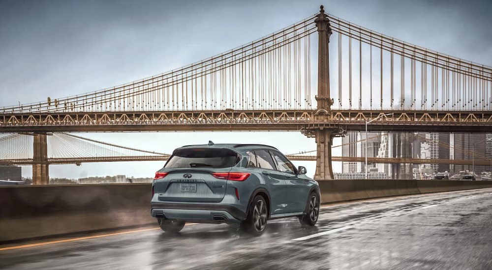 A blue 2025 INFINITI QX50 driving near a large bridge.