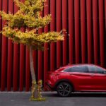 A red 2025 INFINITI QX55 parked near trees and two people walking.