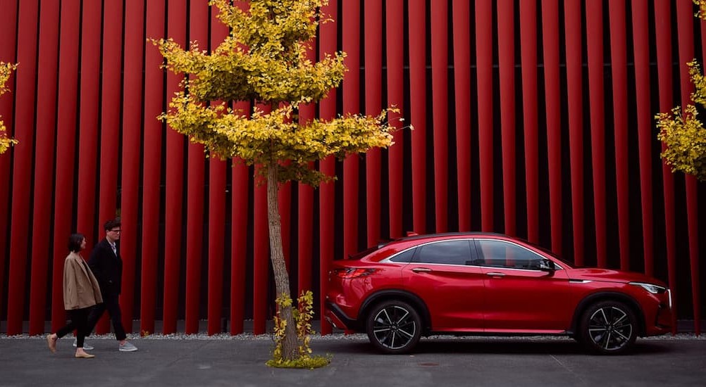A red 2025 INFINITI QX55 parked near trees and two people walking.