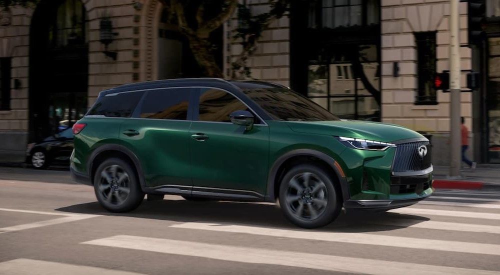 A green 2026 INFINITI QX60 driving in a city.