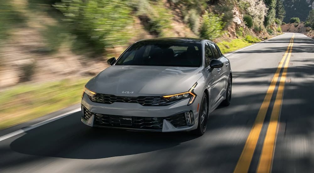 A gray 2025 Kia K5 driving to a Kia dealer.