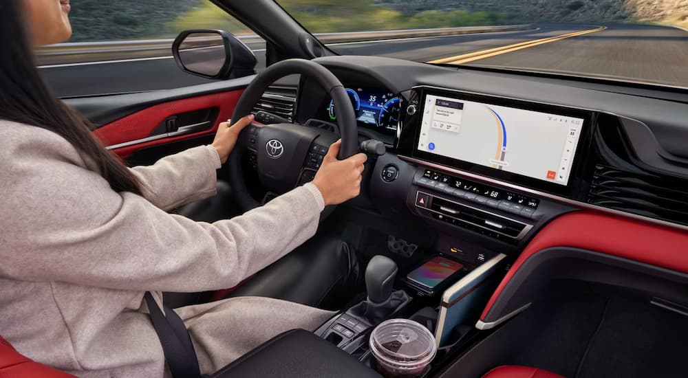 A woman driving a 2026 Toyota Camry with black and red interior down a highway