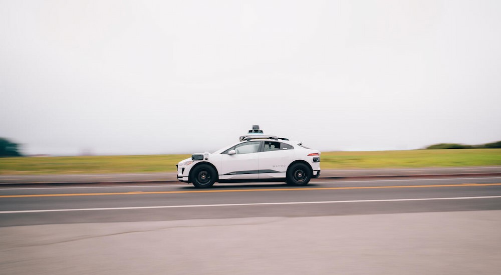 A white Waymo robotaxi driving on a highway.