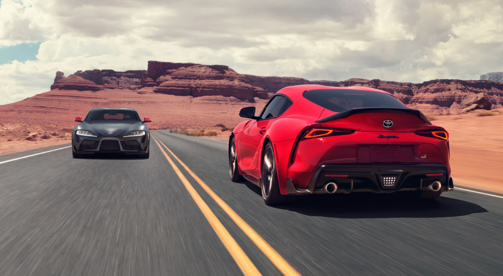 Two 2026 Toyota Supra GR's drve past each other on a desert road.