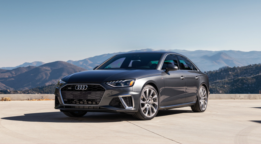 A metallic grey 2025 Audi S4 parked in an empty lot in front of mountains.