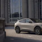 A tan 2025 Ford Mustang Mach-E parked near a stone building.