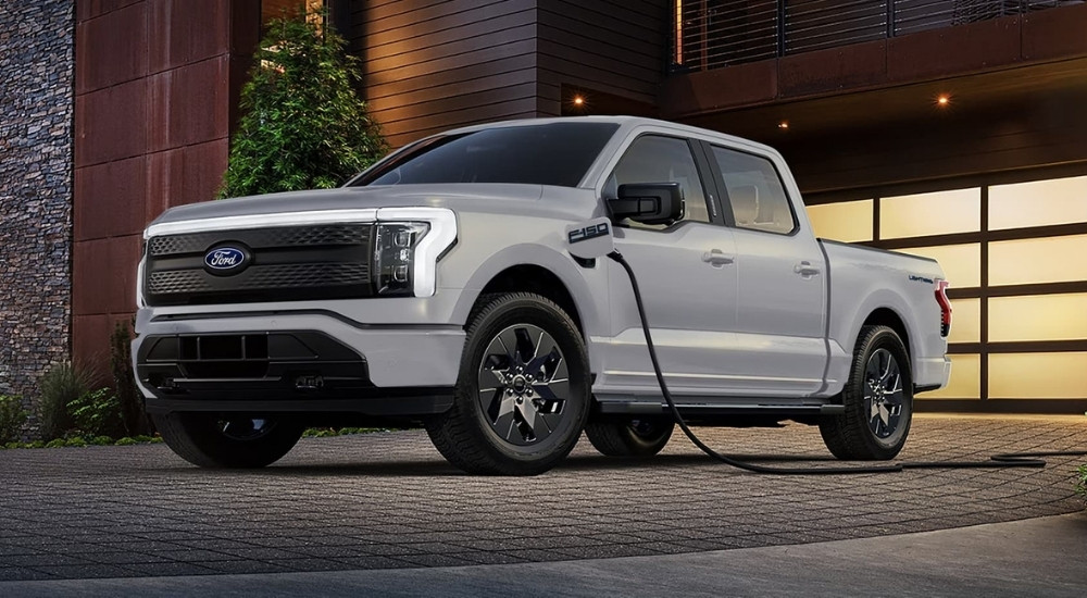 A white 2025 Ford F-150 Lightning charging outside a garage