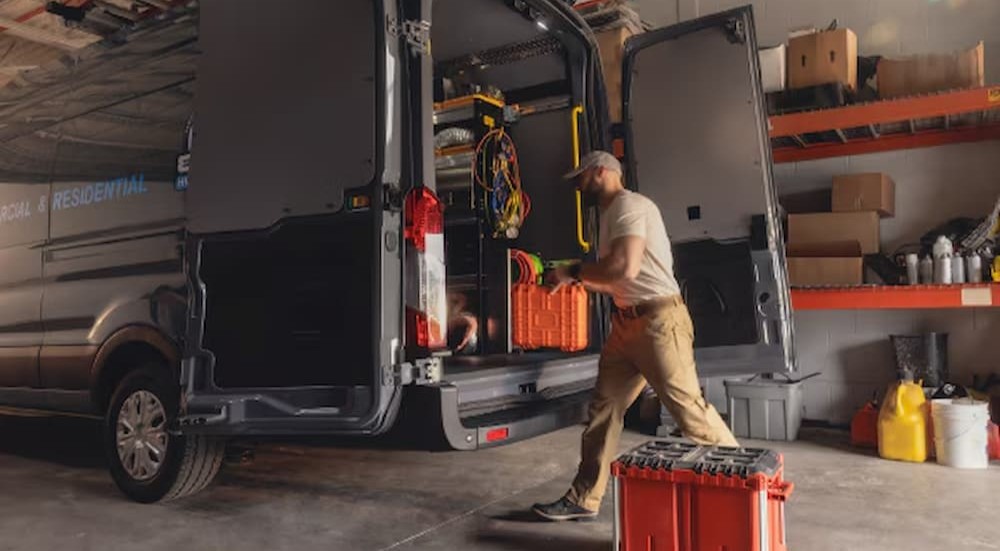 A worker loading equipment onto a gray Ford Transit van.