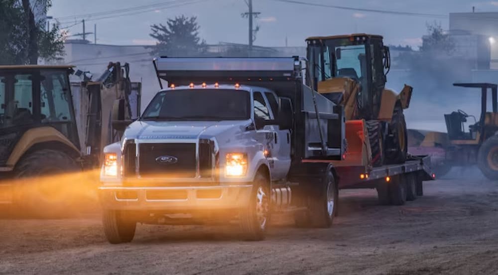 A white Ford Super-Duty towing a trailer to a Ford dealer.