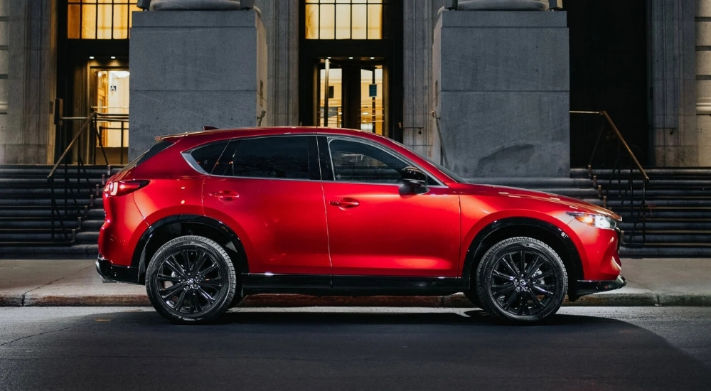 Side of a red 2026 Mazda CX-5 driving through an intersection.