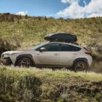 A tan 2026 Subaru Crosstrek Hybrid driving uphill.