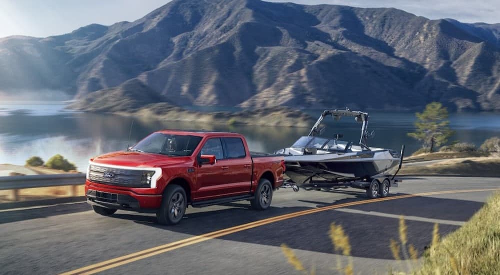 A red 2025 Ford F-150 Lightning towing a boat.