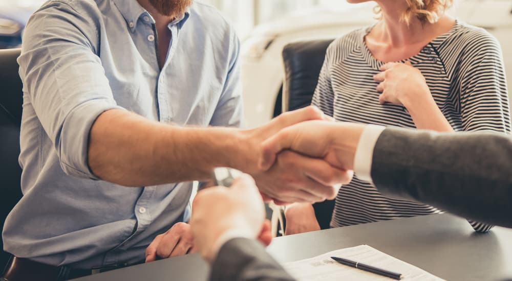 A dealer and a man handshaking over a car purchase