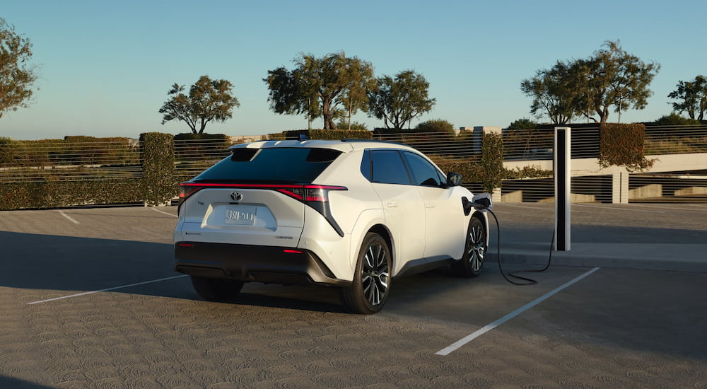 A White 2026 Toyota bZ plugged in to the charger in a parking lot.