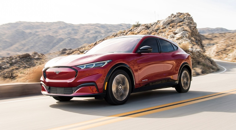 A red 2021 Ford Mustang Mach-E is shown driving by mountains.