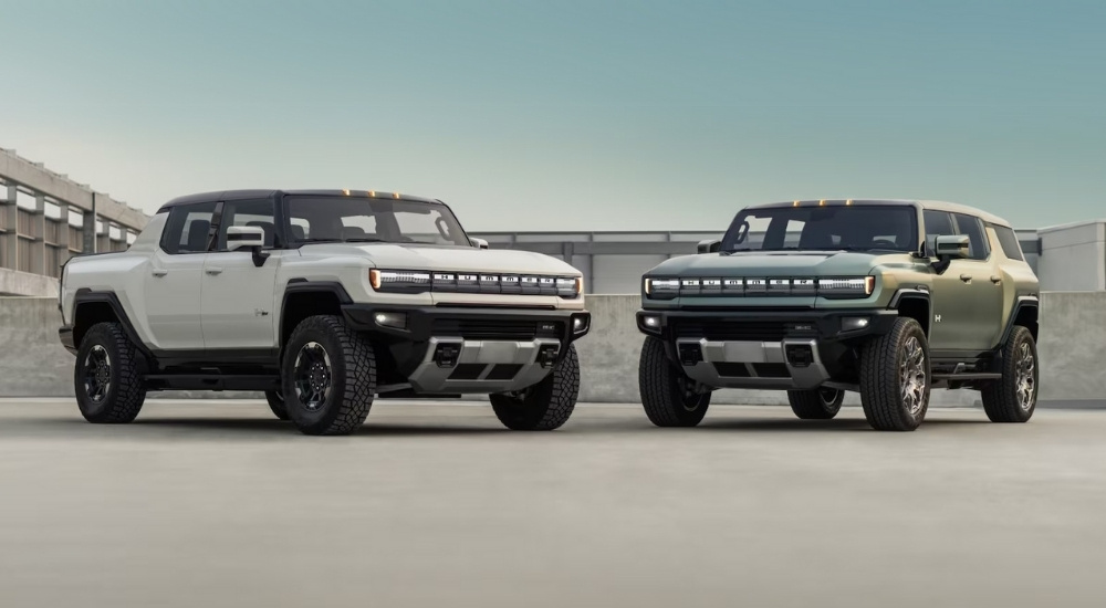 A white and a green 2025 GMC Hummer EV parked next to each other on concrete.