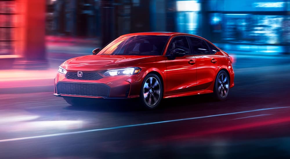 Red 2026 Honda Civic Sedan Hybrid driving down a street.